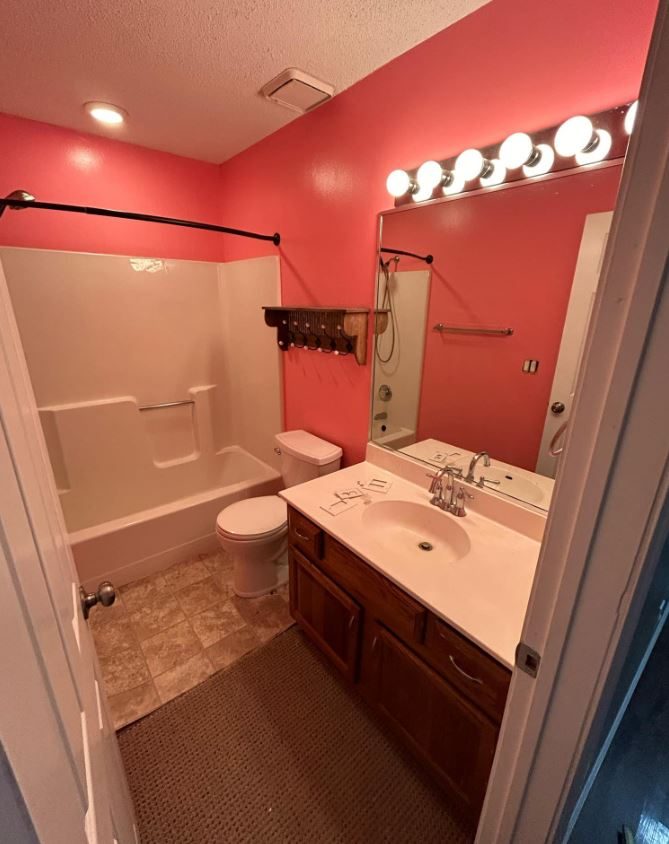 Bathroom before remodeling with a fiberglass tub-shower, coral walls and a wood vanity