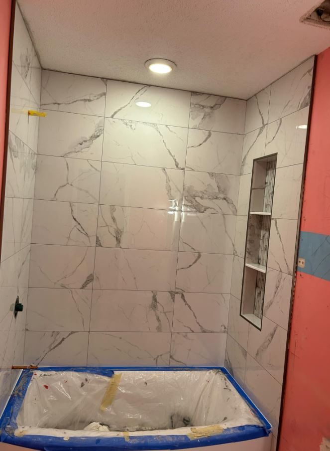 Tub surround tiled in white marble-look porcelain with a recessed niche while the tub is protected
