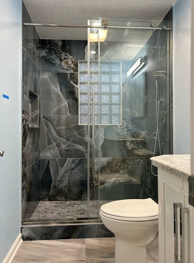 Finished walk-in shower with dark marble-look wall tile, a glass block window and a sliding glass door